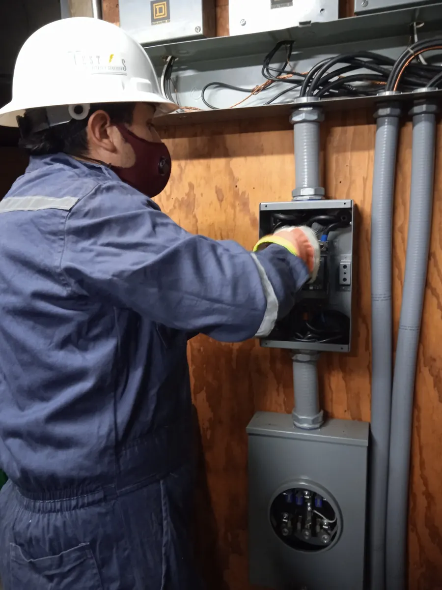 Técnico de TEST con casco blanco instalando un tablero eléctrico y su medidor