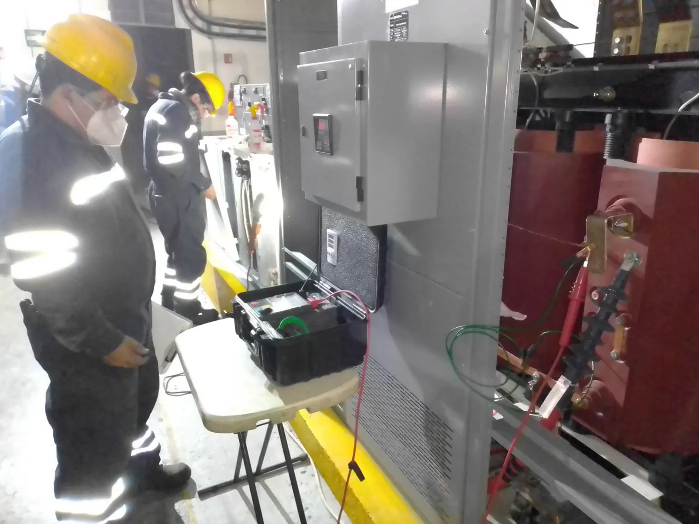 Técnicos con chaleco reflejante realizando pruebas a un transformador seco con equipo de medición