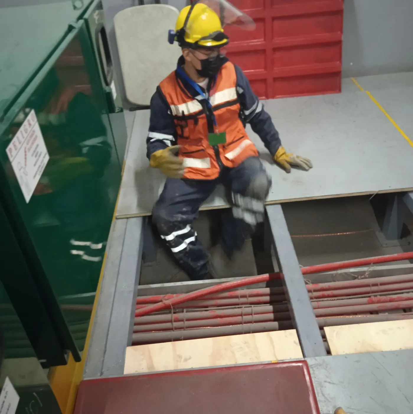 Técnico con chaleco naranja dentro de un registro de piso con cableado de potencia